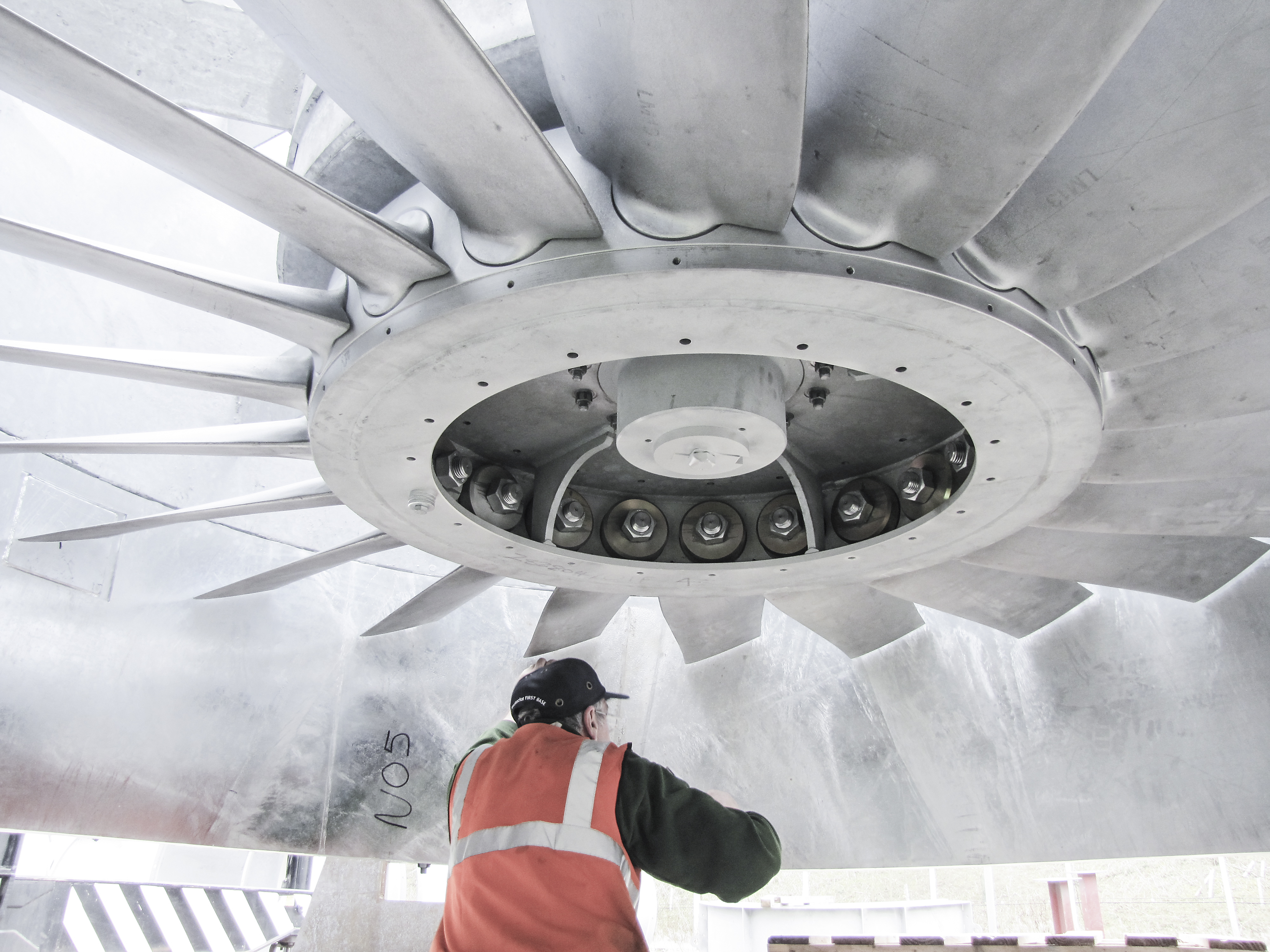 Photo shows a man in an orange hi-vis vest working on a large new exhaust fan